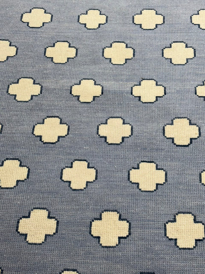 A close-up of a woven textile pattern featuring cream-colored geometric cross motifs on a slate blue-gray background.