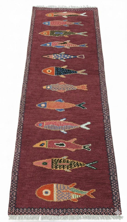 Full view of handmade fish runner rug featuring colorful fish designs on a deep red background with fringe edges.
