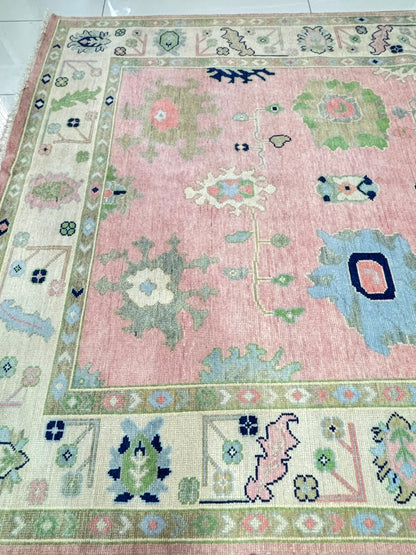 Full view of handmade blush pink Oushak area rug with traditional floral pattern