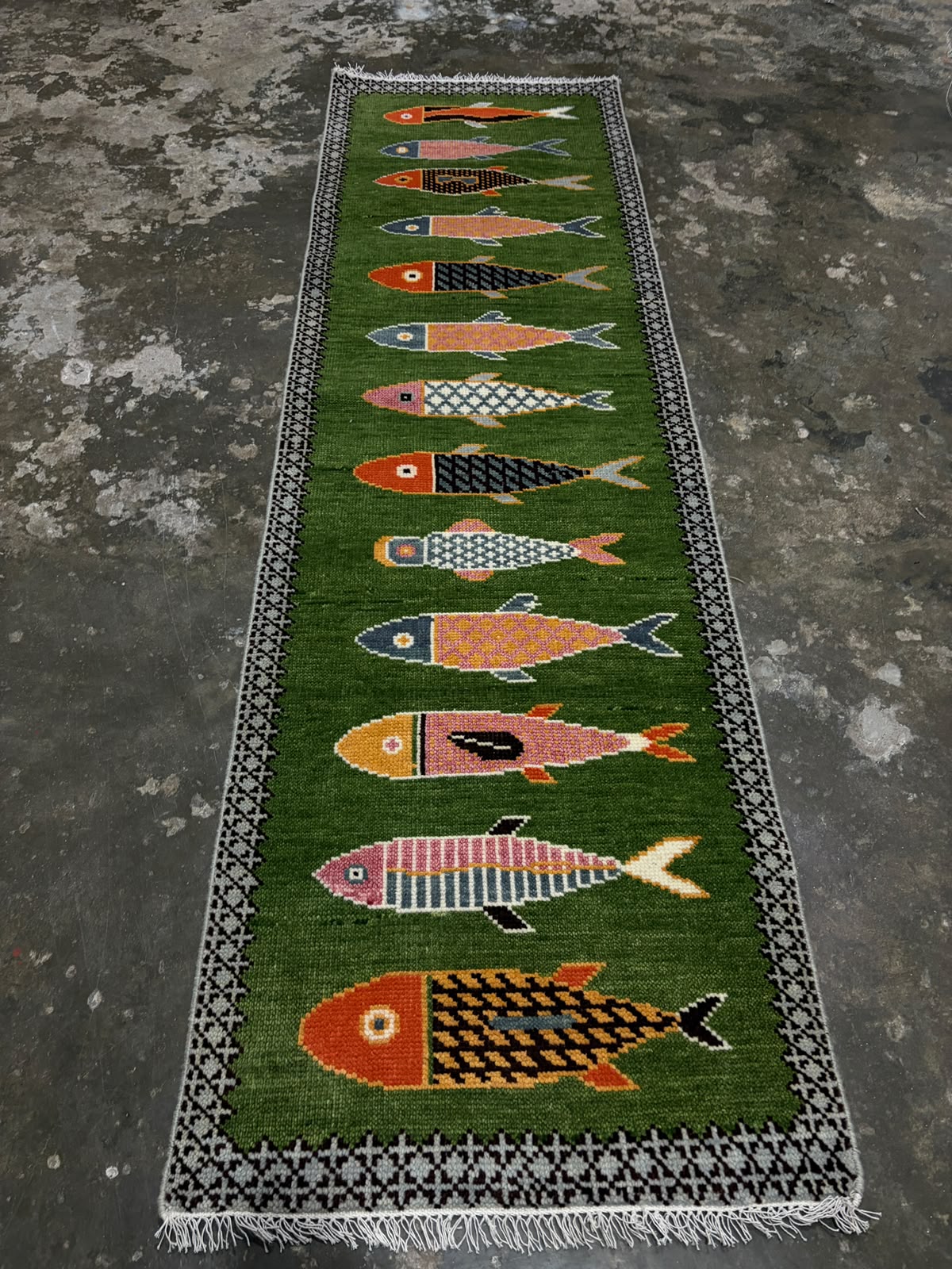 Hand-knotted green wool runner rug with colourful fish motifs and geometric border