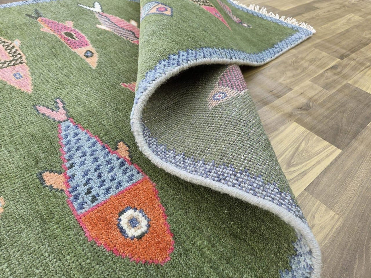 Curled green fish rug showing colorful motifs, blue edging, cream fringe and the reverse side.