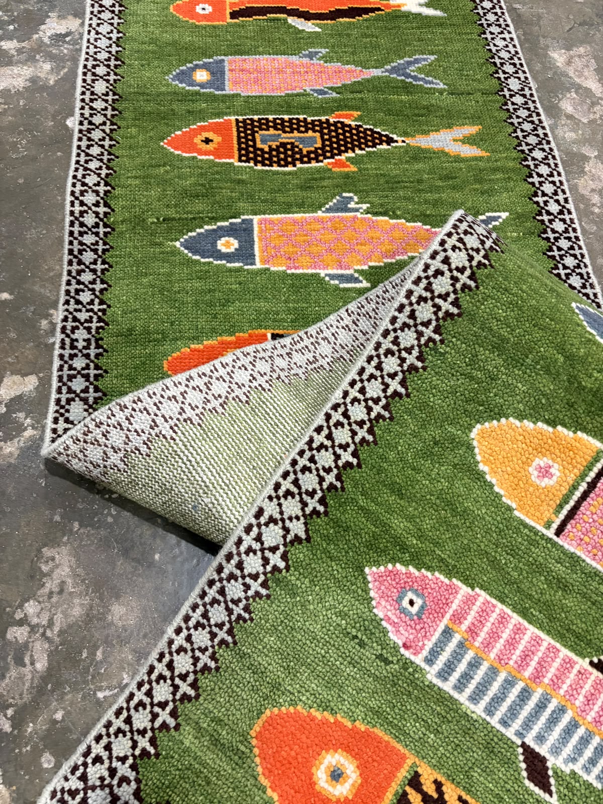 Reverse side of a hand-knotted green wool fish runner rug showing its construction