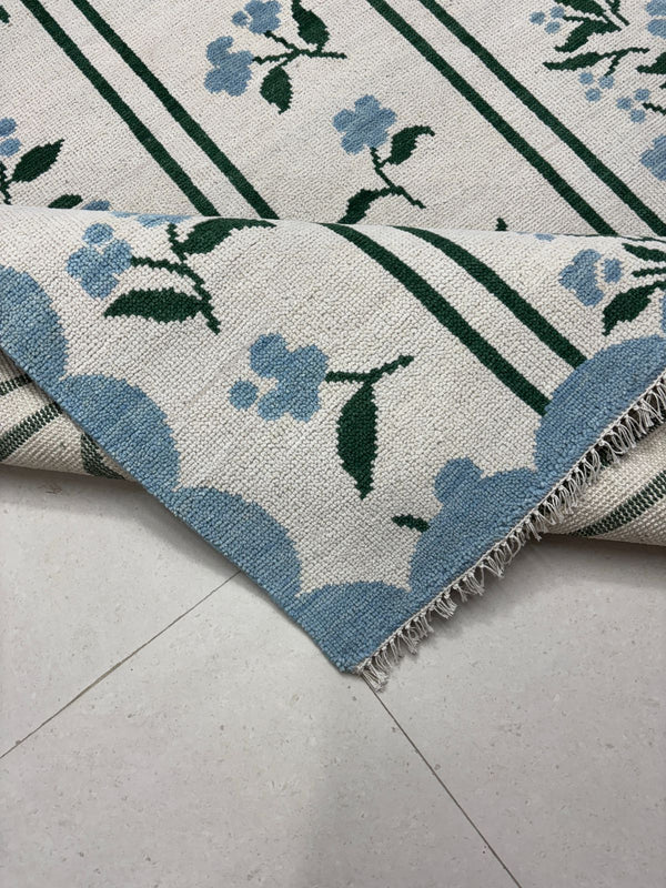 Handmade ivory area rug with blue floral motifs and green striped pattern in modern botanical design