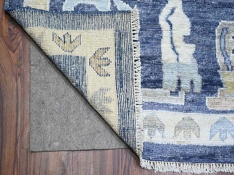 Backside of handmade blue wool rug displaying artisan weaving and cotton backing.