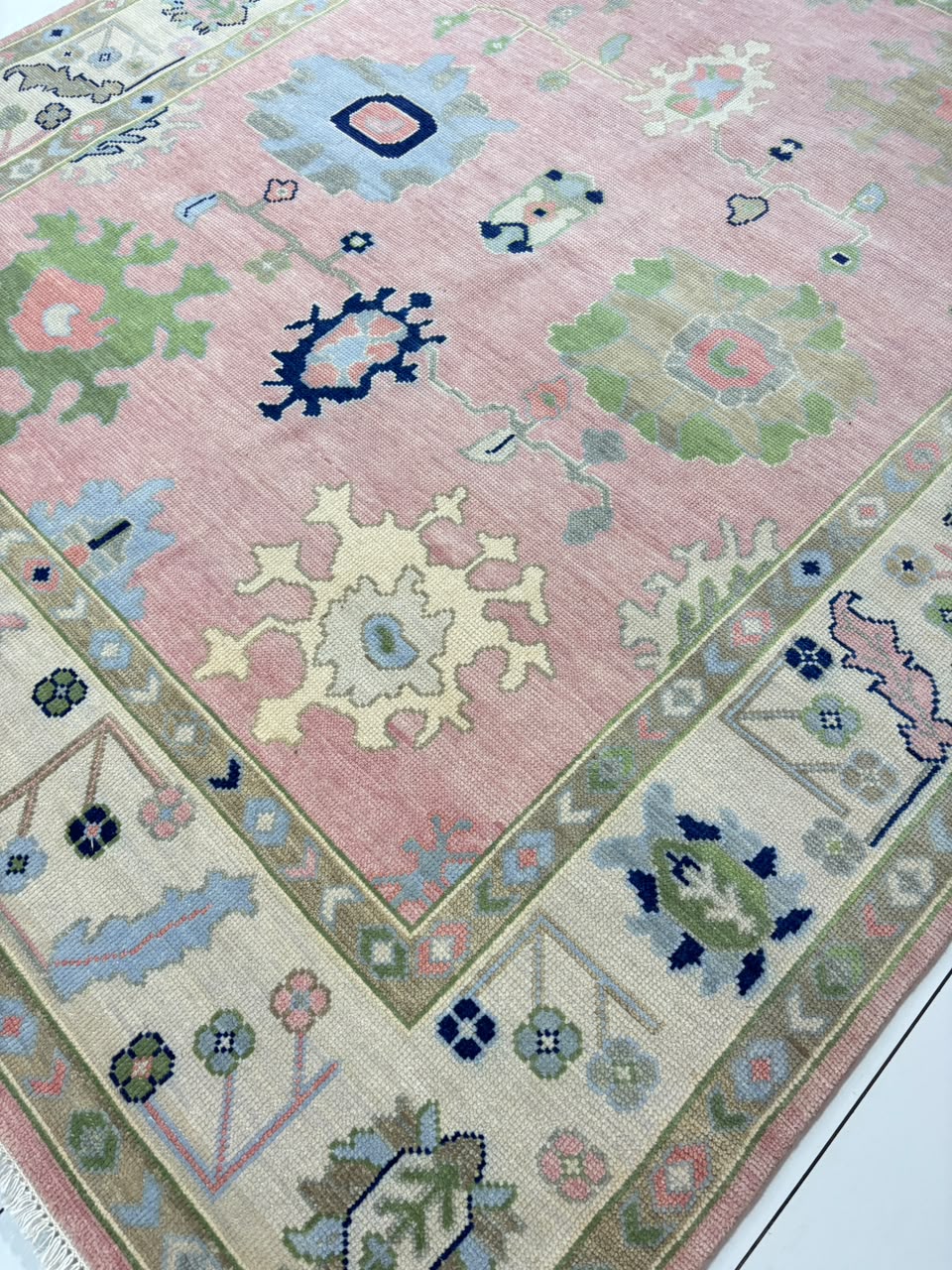 Handmade blush pink Oushak wool area rug with ivory border and sage green floral motifs for living room decor