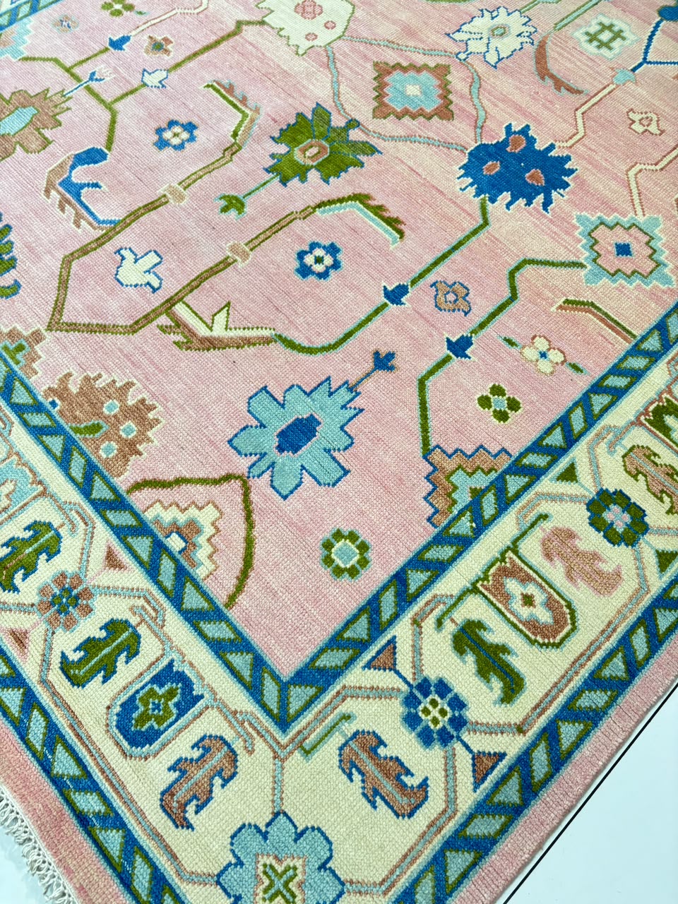 Handmade blush pink Oushak wool rug with blue floral motifs and vintage Turkish design.