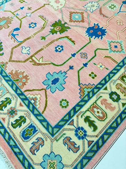 Handmade blush pink Oushak wool rug with blue floral motifs and vintage Turkish design.
