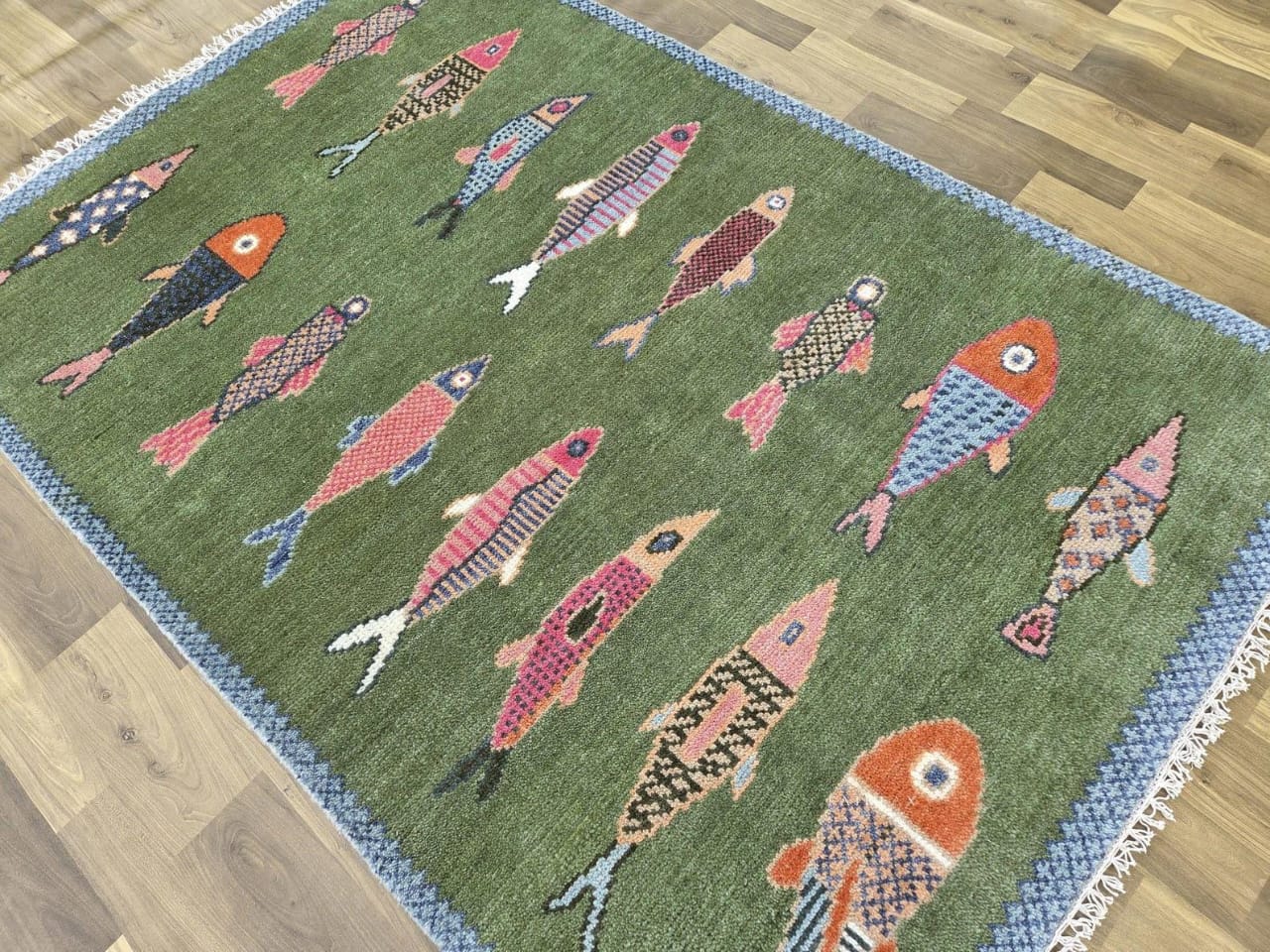 Handmade green coastal fish rug displayed on wooden floor