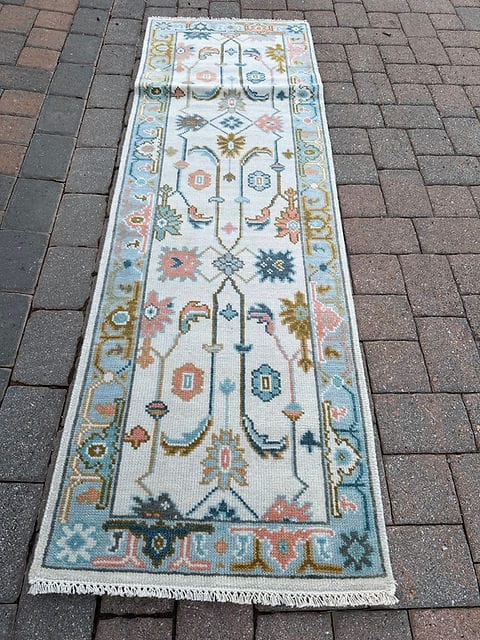 Full view of a handmade vintage Oushak hallway runner with an ivory field and sky blue border.