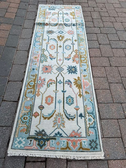 Full view of a handmade vintage Oushak hallway runner with an ivory field and sky blue border.