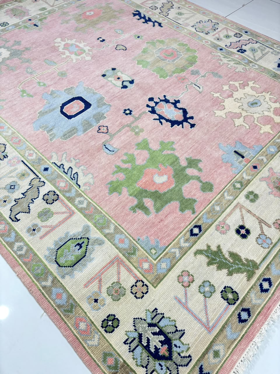 Angled view of handmade vintage blush pink Oushak rug in soft pastel colors
