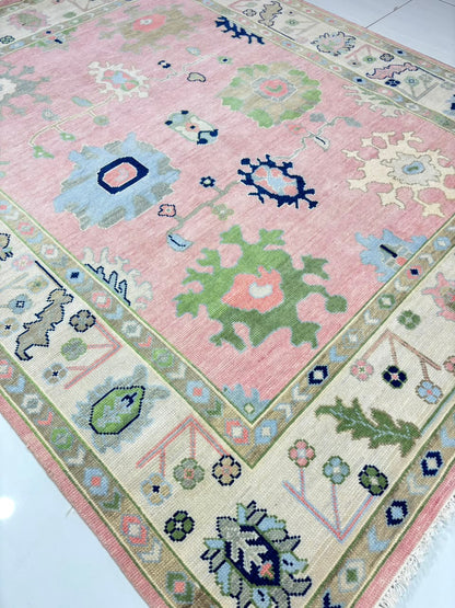 Angled view of handmade vintage blush pink Oushak rug in soft pastel colors