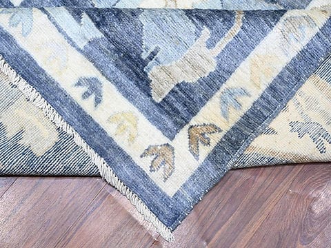 Corner detail of handmade blue Oushak rug with ivory floral border and fringe.