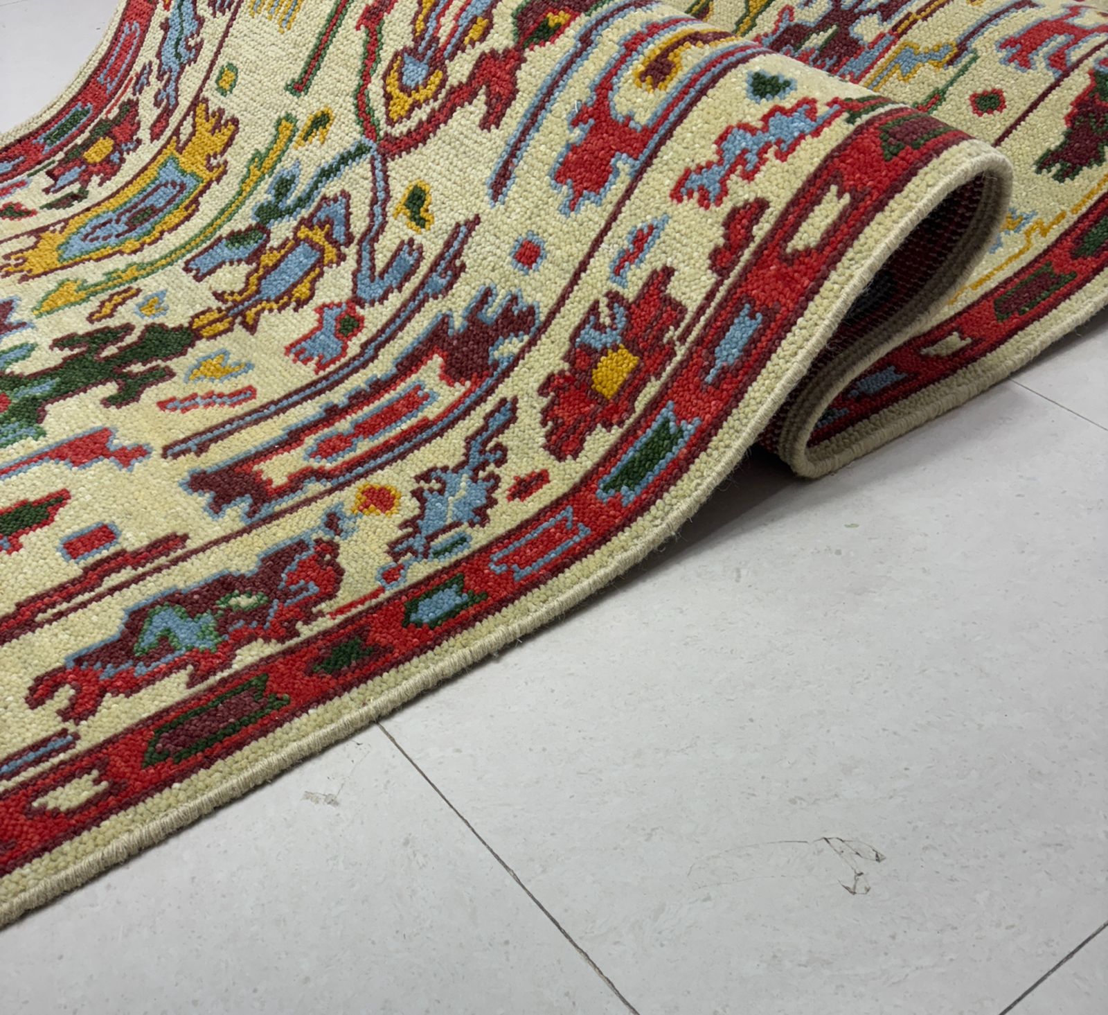 Folded cream and red Oushak runner rug displaying thickness and texture