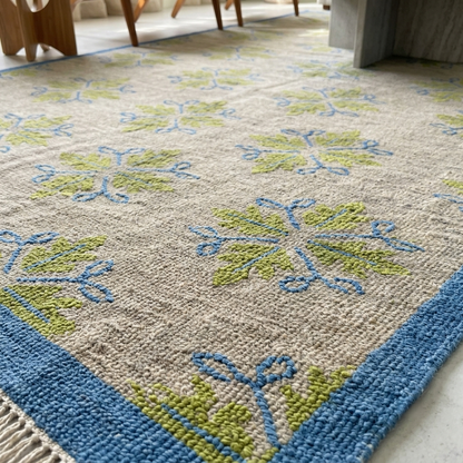 Handmade ivory wool area rug with sage green botanical pattern and blue border styled in a modern living room