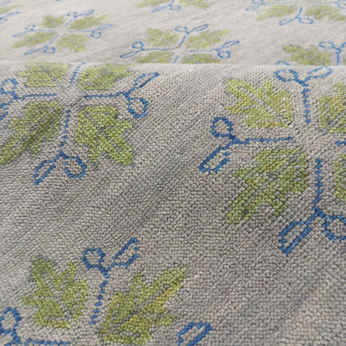 Close-up texture of handmade wool botanical rug in ivory, sage green and blue