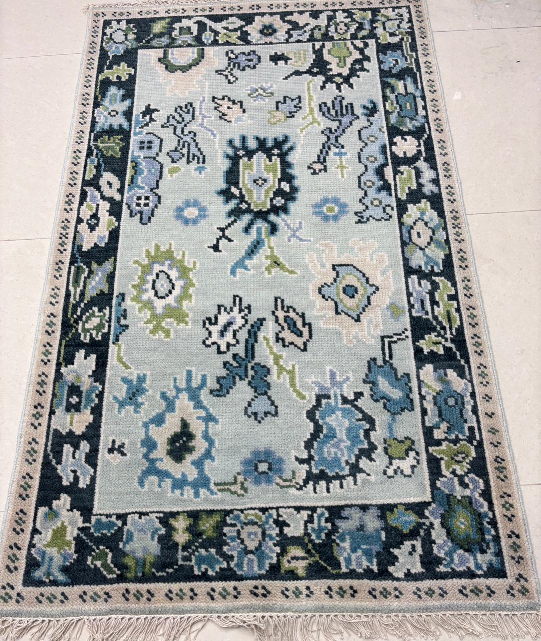 Handmade Scandinavian folk art wool rug with ice blue background, charcoal floral border and sage green accents.