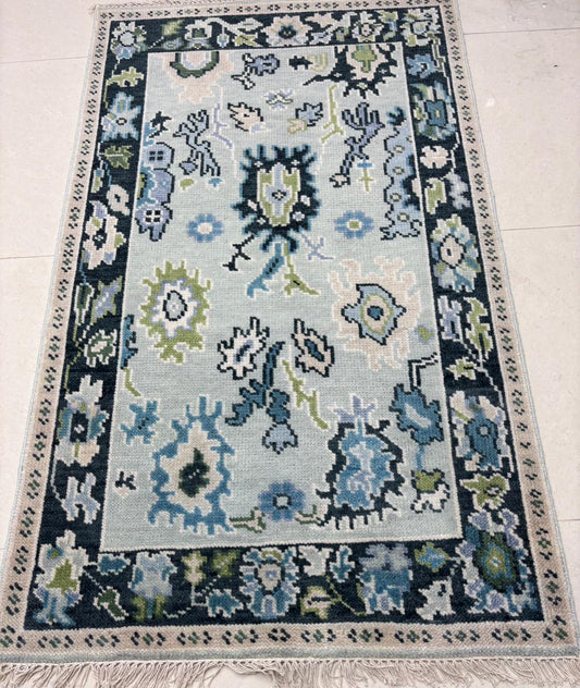 Handmade Scandinavian folk art wool rug with ice blue background, charcoal floral border and sage green accents.