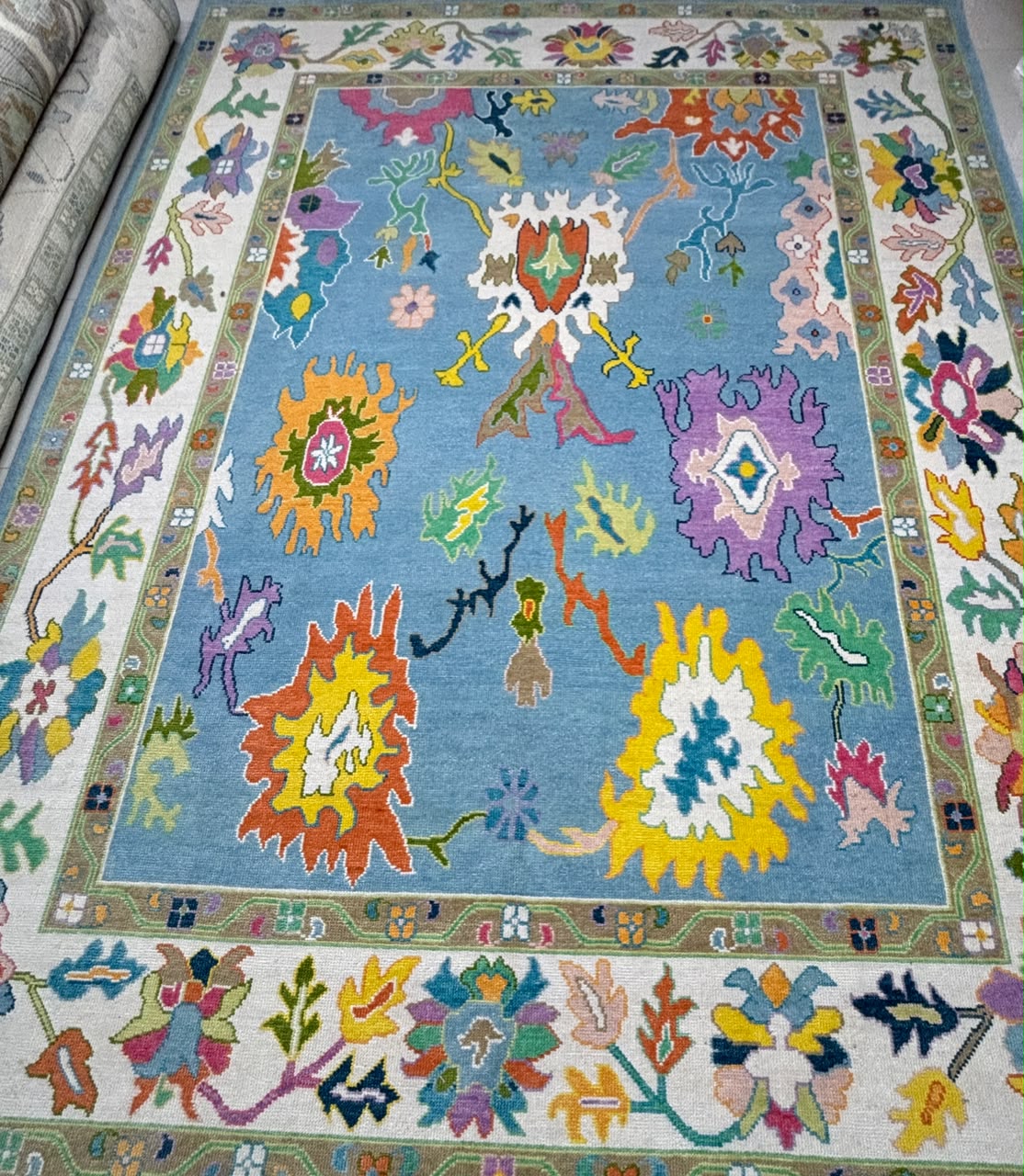 Handmade sky blue contemporary Oushak wool rug with colorful botanical motifs and ivory floral border