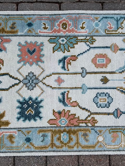 Handmade vintage Oushak runner rug close-up featuring ivory wool with pastel floral motifs and a sky blue border.