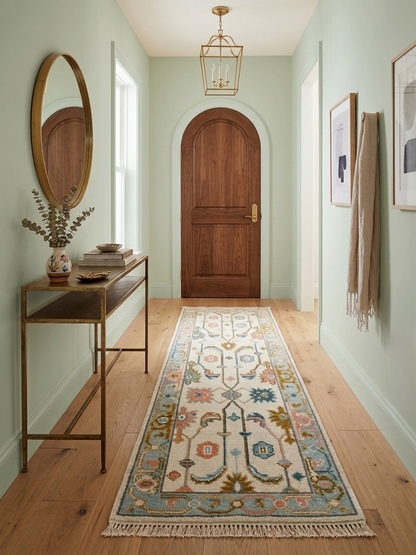 Handmade vintage Oushak runner rug in an entryway hallway featuring an ivory background, soft blue border, and traditional pastel motifs, handcrafted from wool.