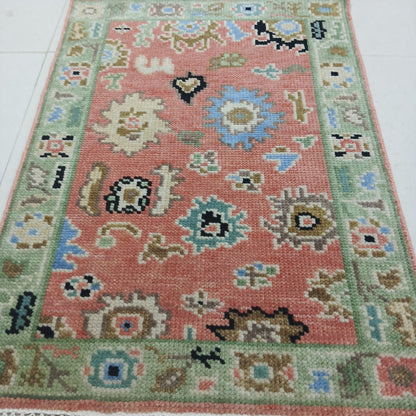 Handwoven Turkish Oushak wool rug with salmon pink field and green border, traditional Anatolian design
