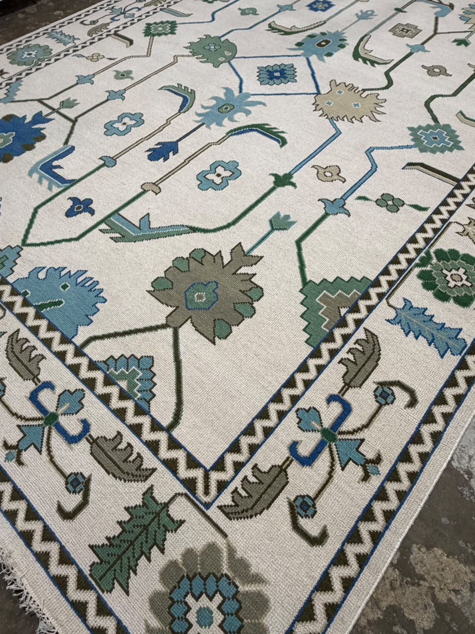 Decorative blue and green border with ivory fringe on a traditional floral rug.