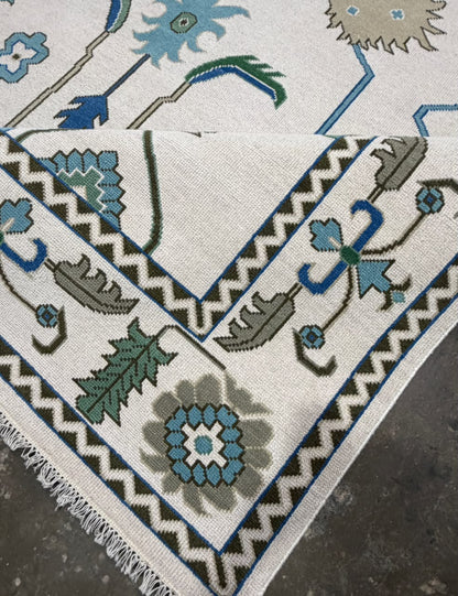 Folded corner of an ivory rug showing the reverse side and geometric border.