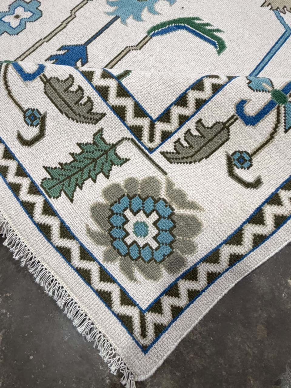 Folded corner of an ivory rug showing the reverse side and geometric border.