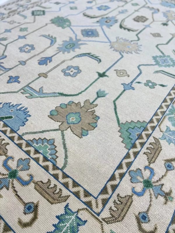 Close-up of handmade ivory blue Oushak style wool rug showing detailed floral motifs and artisan weaving.