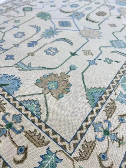 Close-up of handmade ivory blue Oushak style wool rug showing detailed floral motifs and artisan weaving.