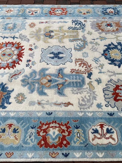 Close view of ivory and blue Oushak rug pattern with floral medallions and decorative elements