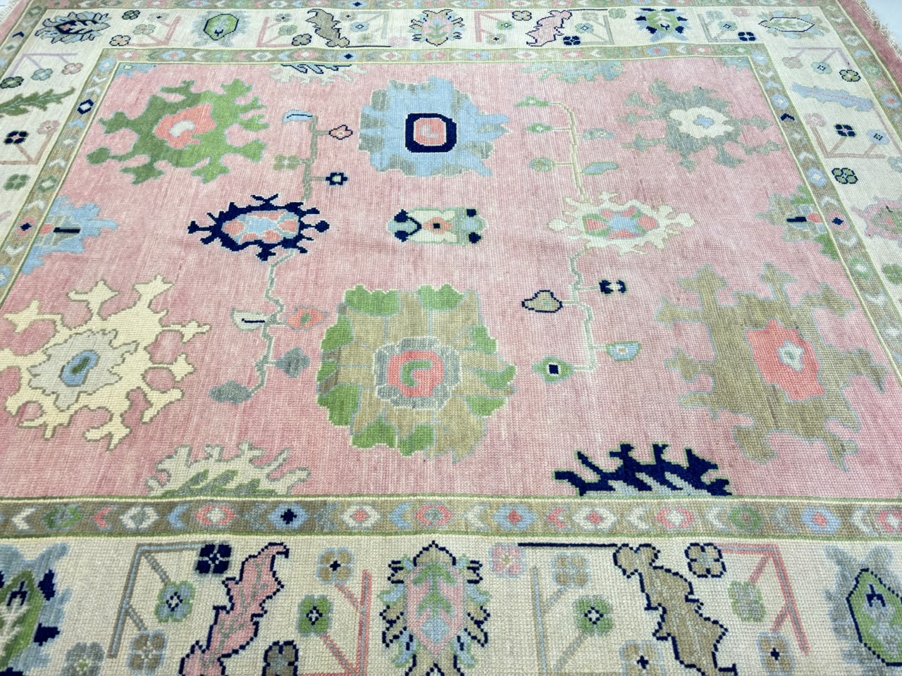 Decorative ivory border with floral motifs on handmade blush pink Oushak rug