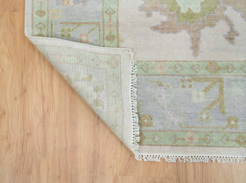 Corner of ivory floral rug showing the reverse side, decorative border and fringe.
