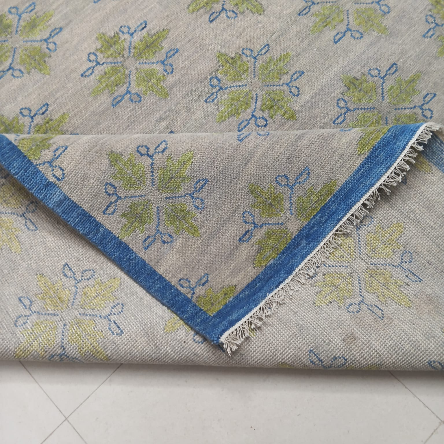 Detailed view of handcrafted ivory wool rug featuring botanical motifs in sage green and blue
