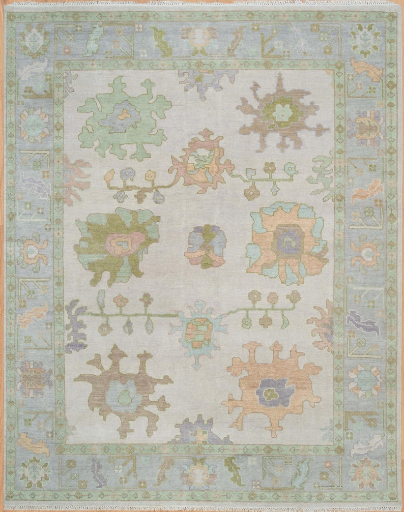 Full view of ivory and mint green floral Oushak-style rug with pastel botanical motifs and decorative border.