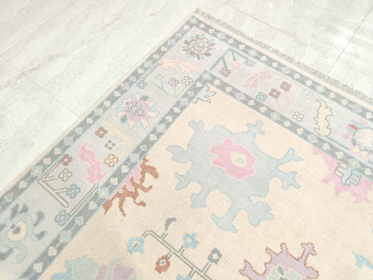 Angled view of ivory Oushak rug with soft blue and blush design