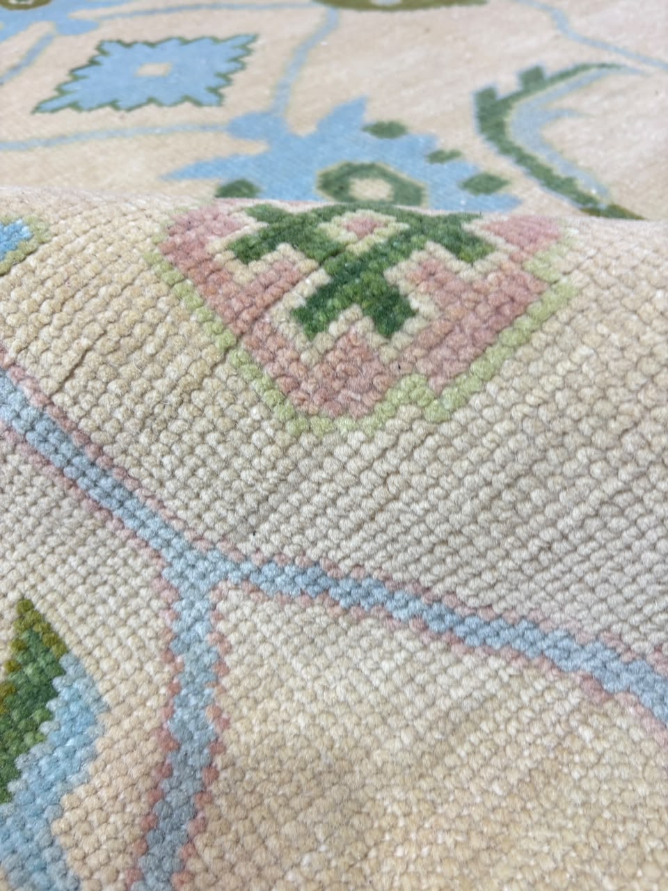 Close-up of ivory blue floral border on handmade Oushak wool rug.