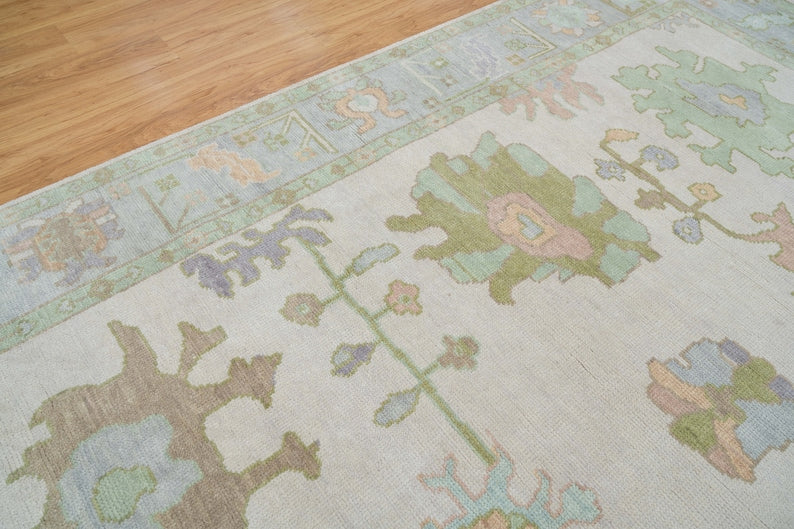 Close-up of pastel floral rug showing sage green, dusty blue, pink and beige botanical motifs.