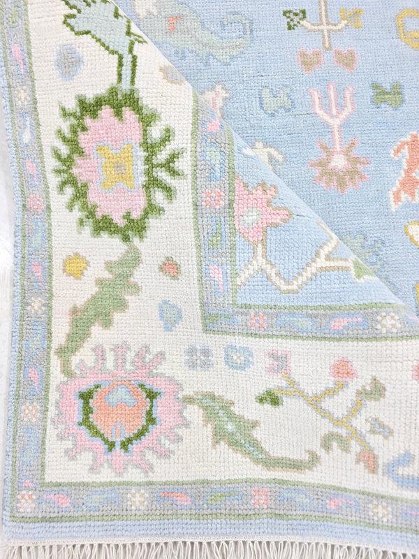 Light blue vintage floral rug showing woven texture, pastel flowers and ivory border