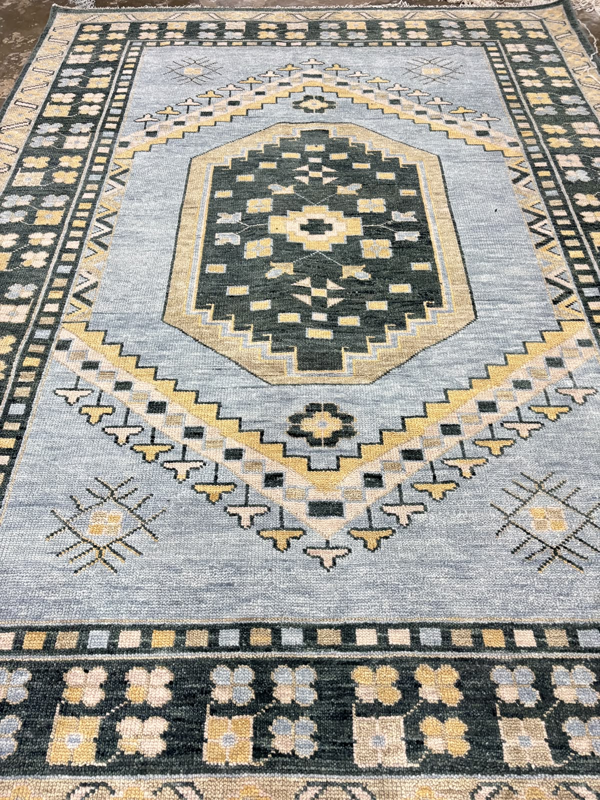 Full view of handmade light blue vintage Oushak area rug featuring geometric tribal motifs and charcoal floral border.
