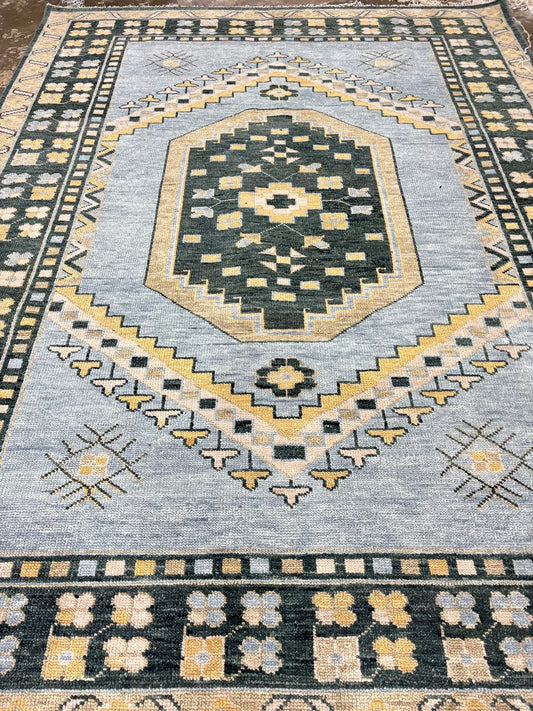 Full view of handmade light blue vintage Oushak area rug featuring geometric tribal motifs and charcoal floral border.