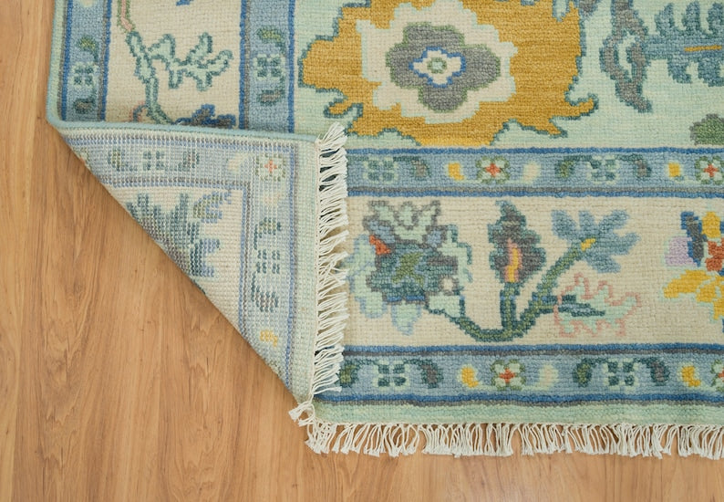 Turned-back corner of a mint green floral Oushak rug showing its reverse weave, border and cream fringe