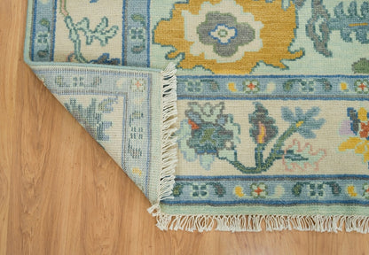 Turned-back corner of a mint green floral Oushak rug showing its reverse weave, border and cream fringe