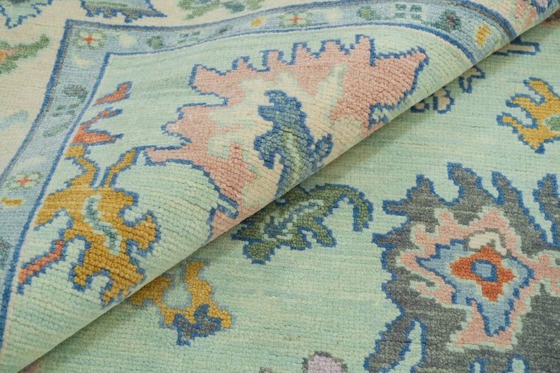 Folded detail of a mint green Oushak rug showing its texture and pink, blue and mustard floral motifs