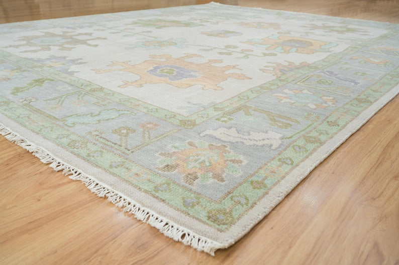 Angled view of ivory floral area rug with mint green border and cream fringe.