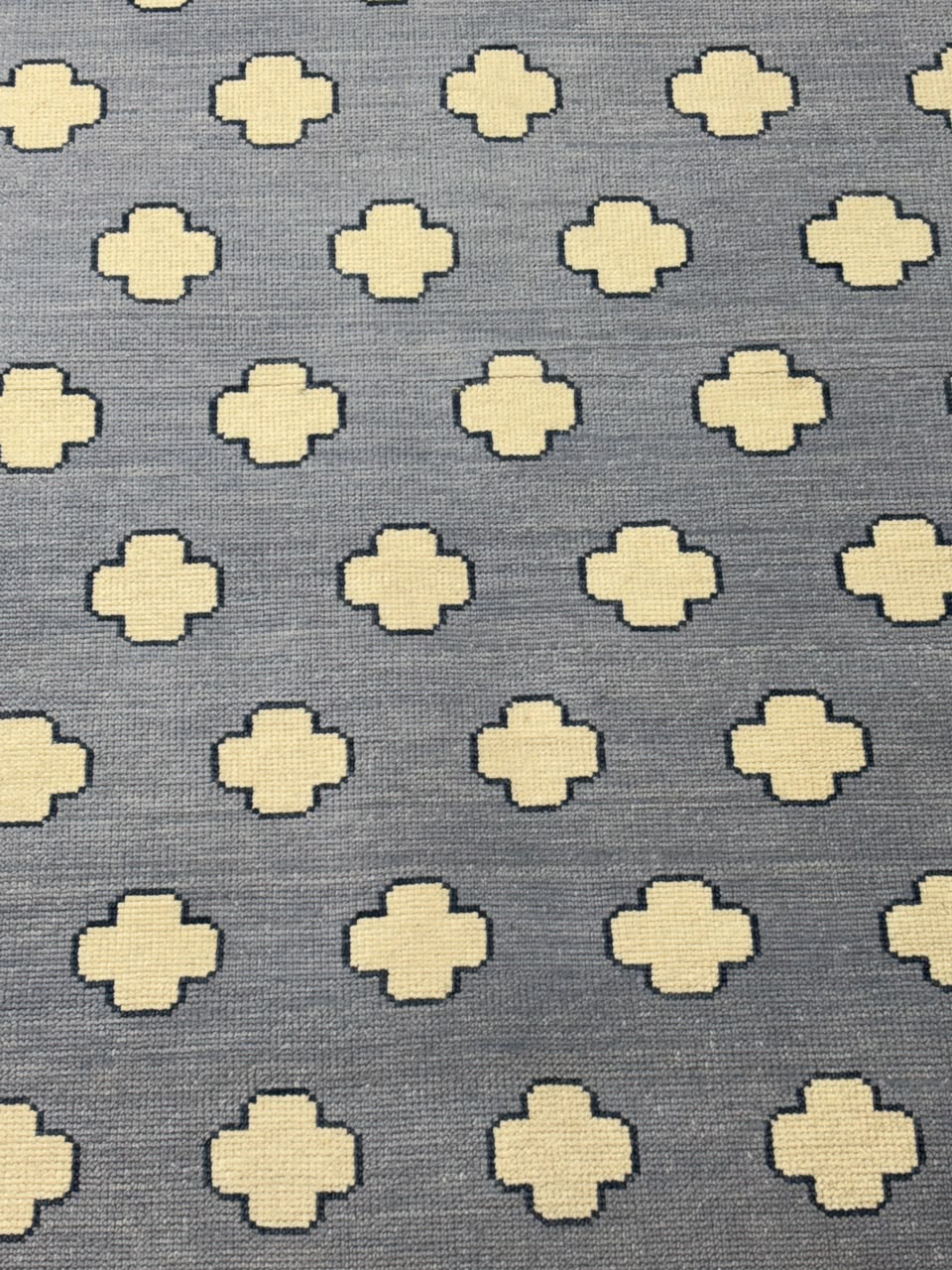 Detailed view of repeating quatrefoil motifs woven into a handmade wool area rug.