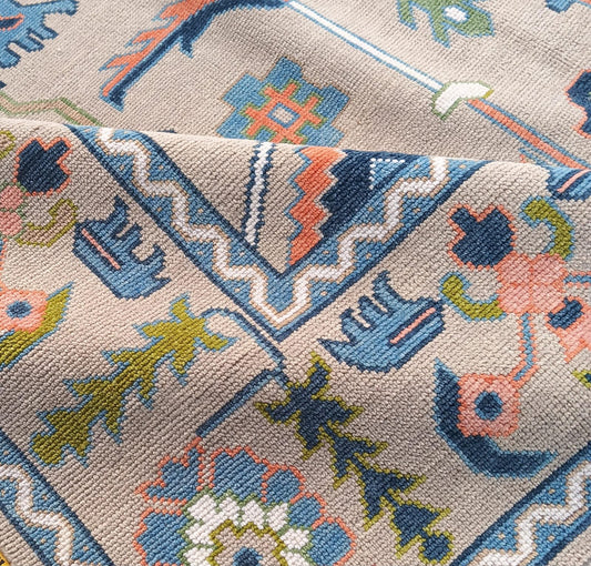 Close-up of folded handmade neutral Oushak wool rug showing premium pile, dusty blue border and traditional geometric details.
