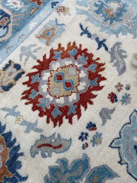 Close up of handmade Oushak rug featuring intricate floral medallion pattern in ivory blue and rust tones