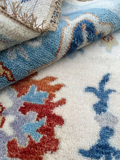 Folded handmade Oushak rug displaying thick wool pile and soft ivory blue floral design